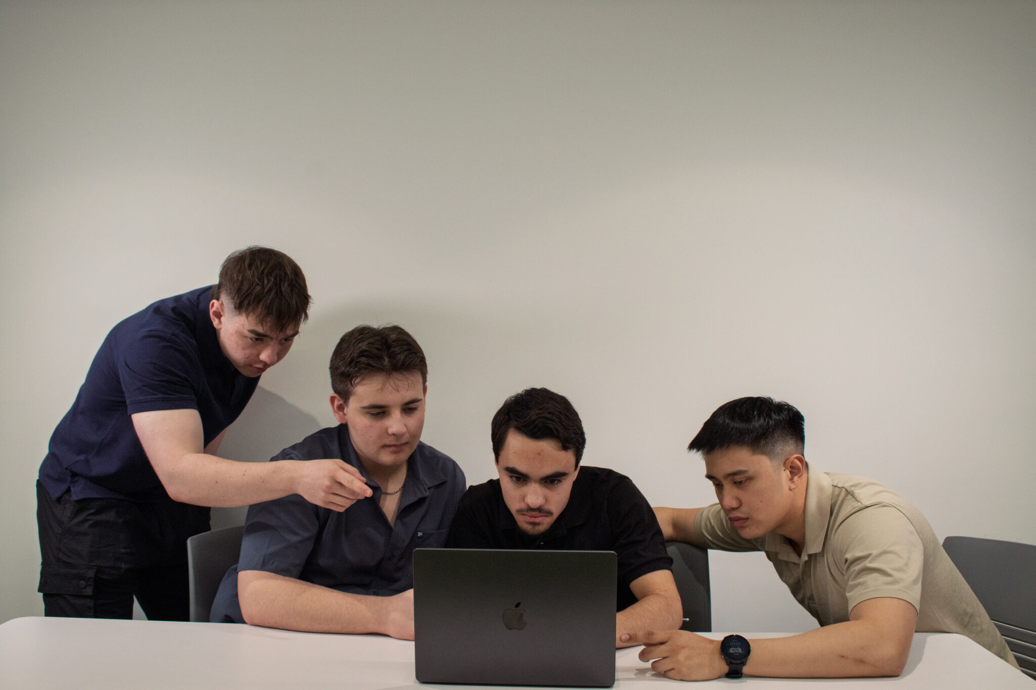 An image of the entire team looking at a laptop with Nate pointing, set against a white background. This photo captures the team in a focused and collaborative moment, showcasing the 'About' us vibe of a dedicated, professional web design team working together.